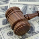 An image focused on the legal side of monetary gains using a gavel and an abundance of American cash as a background.