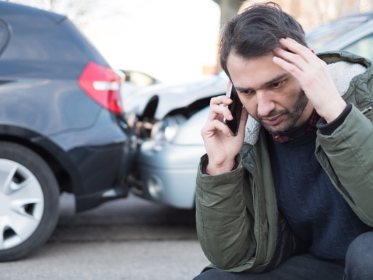 man looking stressed out while talking on the phone after a car accident