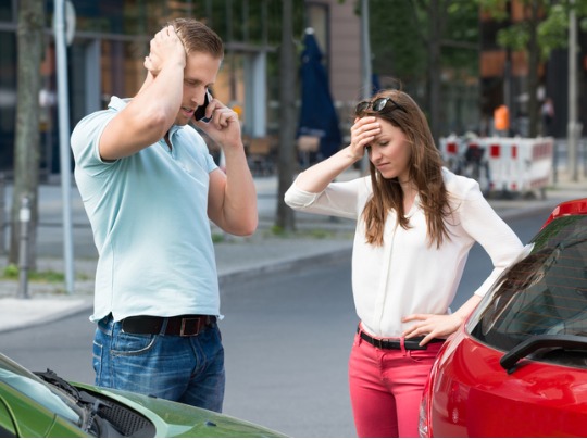 man talking on the phone standing next to a woman after a car accident