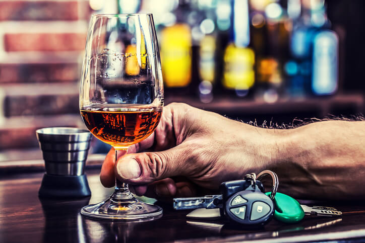 person holding a glass of alcohol with car keys on the counter next to them