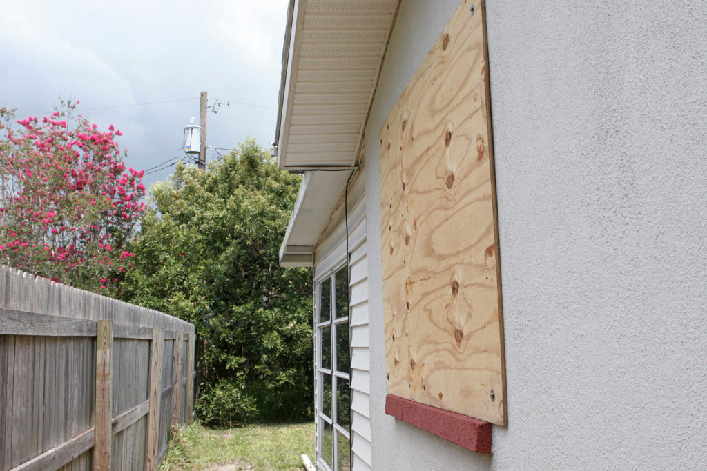 A home with plywood covering the window in preparation for a hurricane. The storm clouds are gathering in the sky. Horizontal view.