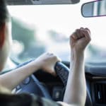 A angry adult sitting in the car, holding a fist up at another driver.