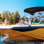 boy and gifl on teh front of a small boat while dad drives