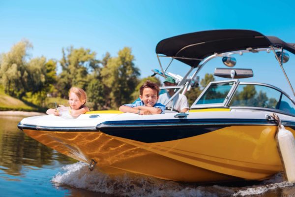 boy and gifl on teh front of a small boat while dad drives