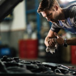 Young mechanic wiping his hands while repairing car engine in auto repair shop.