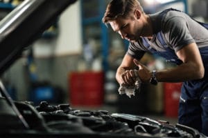 Young mechanic wiping his hands while repairing car engine in auto repair shop.
