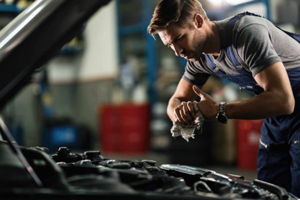 Young mechanic wiping his hands while repairing car engine in auto repair shop.