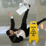 Senior businessman falling on wet floor in front of caution sign