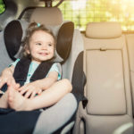 Beautyful smiling baby girl fastened with security belt in safety car seat