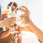 Group of happy friends cheering with tropical cocktails at boat party - Young people having fun in caribbean sea tour - Youth and summer vacation concept - Focus on bottom hands glass